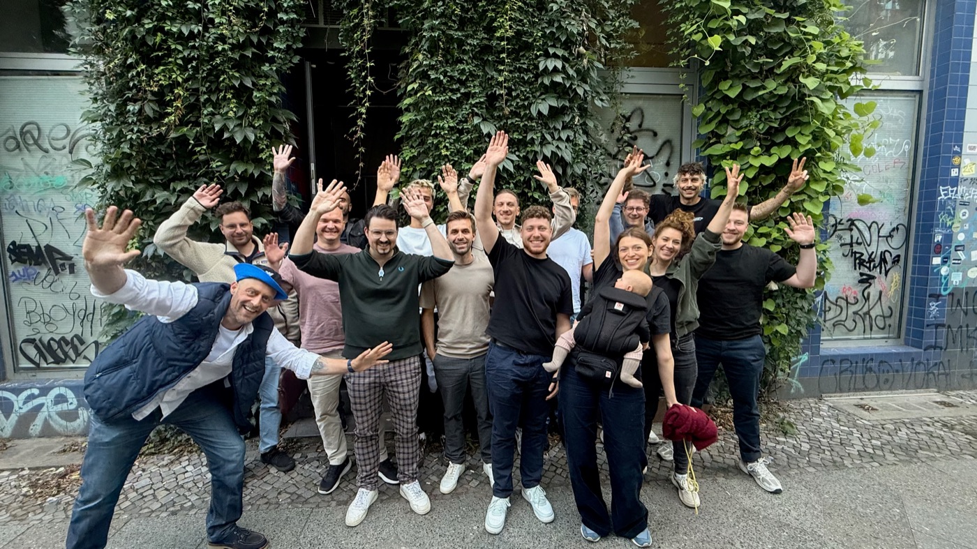 Gruppenfoto der Watch Party Berlin 2025 vor einer efeubewachsenen Fassade, alle winken in die Kamera